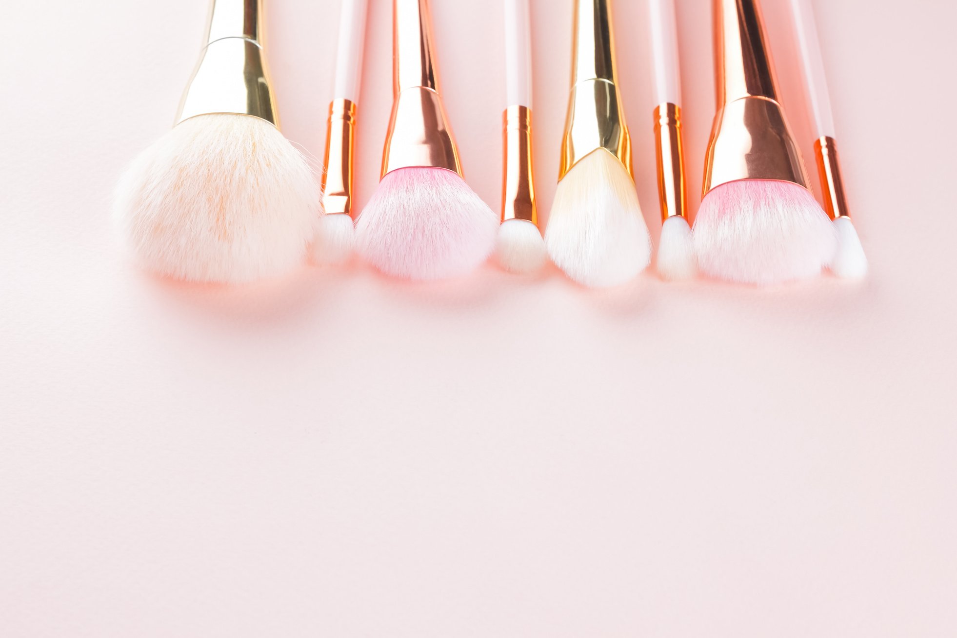 Makeup brushes on pink background. Set of golden makeup brushes,